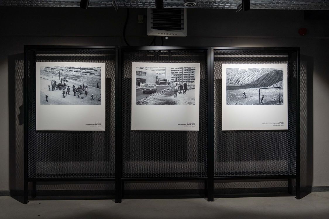 Trzy duże, czarno-białe archiwalne fotografie przedstawiające dawne życie miejskie i robotnicze, zawieszone na metalowych, siatkowych panelach ekspozycyjnych