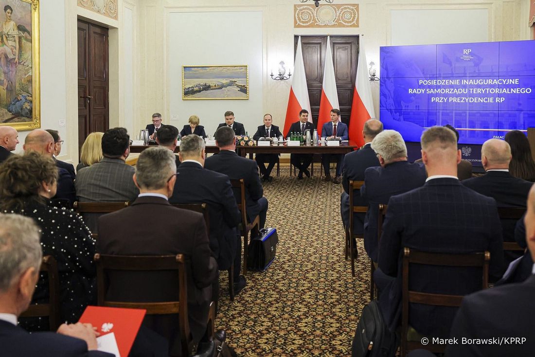 na sali konferencyjnej siedzą włodarze gmin przed nimi stół prezydialnym przy nim 6 meżczyzn po prawej stronie trzy biało-czerwone flagi