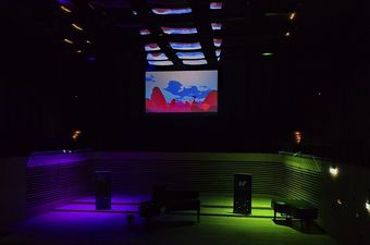 Grafika wyświtlona nad scena oświetloną róznymi kolorami śiwateł.