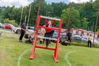 zawodnik z czerwono-czarnym stroju wspoina sie na czerwoną przeszkode ze szczeblami 