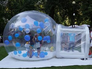 Dzieci bawiące się wewnątrz wielkiej, przezroczystej dmuchanej kuli wypełnionej niebieskimi balonami podczas festynu
