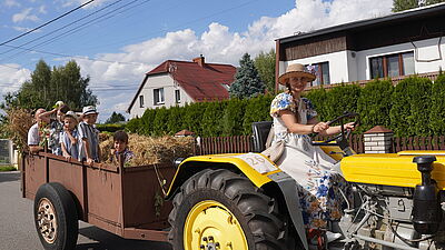 Pani za kierownicą traktoru, wiozącego przyczepe z dziećmi.