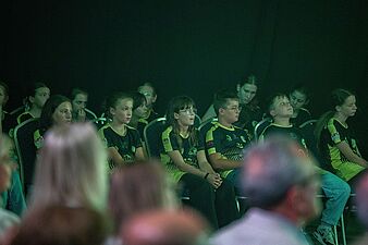 Grupa dzieci siedzi na krzesłach podczas uroczystości