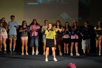 dziewczyna w żółtej koszulce i czarnych spodenkach śpiewa za nią inni uczniowie