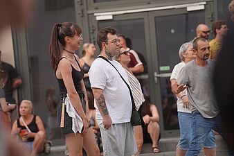 Młoda kobieta w czarnym topie i mężczyzna w białym koszulce stojący wśród uczestników imprezy plenerowej