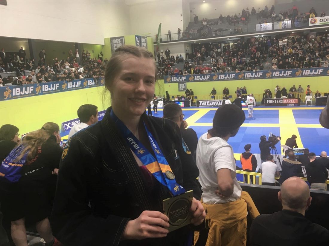 Dziewczyna prezentuje medal, z nią widok hali sportowej, na trybunach ludzie