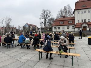 Uczestnicy śniadania wielkanocnego siedzą przy stolikach i jedzą