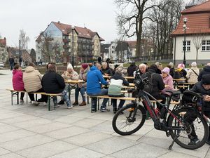 Uczestnicy śniadania wielkanocnego siedzą przy stolikach i jedzą na pierwszym planie rower