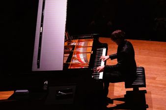 Pianista grający na fortepianie widziany z boku.