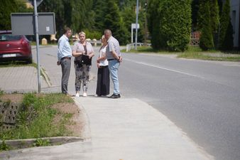 Trzyosobowa grupa w tym Michał Urgoł Prezydent Miasta rozmawia na ulicy Tysiąclecia w słoneczny dzień
