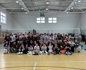 Grupowe zdjęcie złotych młodzików z medalami, trenerami, rodzinami, kibicami i działaczami na tle siatki w geście okrzyku radości