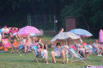 Widzowie odpoczywający na leżakach pod kolorowymi parasolami plażowymi na trawiastym terenie.