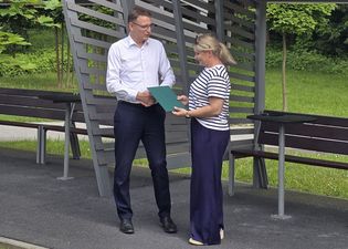 Michał Urgoł Prezydent Miasta ubrany w białą koszulę przekazuje dyplom laureatce w bluzce w paski. Oboje stoją na zewnątrz pod zadaszeniem