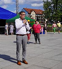 Prezydent Miasta Michał Urgoł przemiawia na placu, z tyłu kolorowe namioty oraz grupka osób
