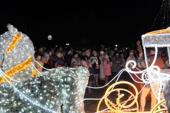 Tłum ludzi obserwujący muzyków występujących przy rozświetlonej dekoracji w kształcie świątecznej karety z końmi