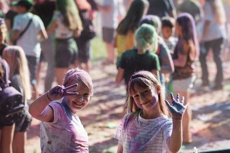 Portret dwóch radosnych dziewczynek pozujących do zdjęcia, umazanych kolorowymi proszkami holi