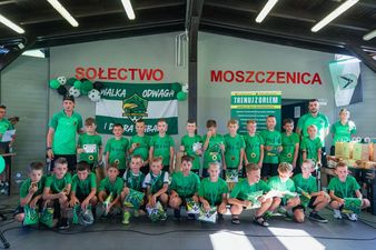 Grupowe zdjęcie zawodników UKS Orzeł Moszczenica w zielonych strojach klubowych, pozujących wraz z trenerami po odebraniu medali i dyplomów podczas festynu