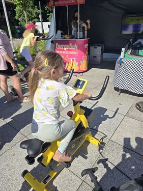 Mała dziewczynka jedzie na żółtym rowerku stacjonarnym wytwarzającym energię na pikniku rodzinnym