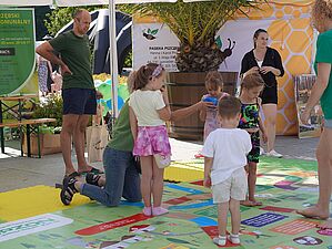 Mata z elementami ekologicznymi, na niej dzieci, wokół dorośli