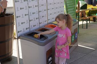Dziewczynka w różowej sukience wrzucająca butelkę do pojemnika na segregację śmieci