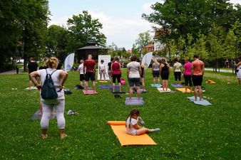 Zajęcia fitness na trawie w Parku Zdrojowym; na pierwszym planie mała dziewczynka siedzi na pomarańczowej macie