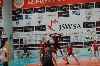 Rozgrywający gospodarzy przed odbiciem piłki, przed nim środkowy plecami do siatki podczas wyskoku w celu zasłonięcia piłki