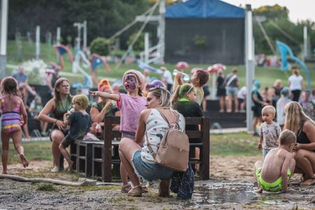 Dzieci i rodzice odpoczywający na piaszczysto-błotnistym terenie rekreacyjnym po festiwalu kolorów