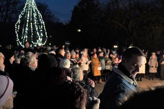Tłum ludzi zebrany nocą w parku. W tle widać dużą, rozświetloną białymi lampkami choinkę