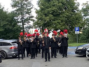 Górnicza orkiestra dęta pod bujnymi drzewami na parkingu, prowadzona przez tamburmajora