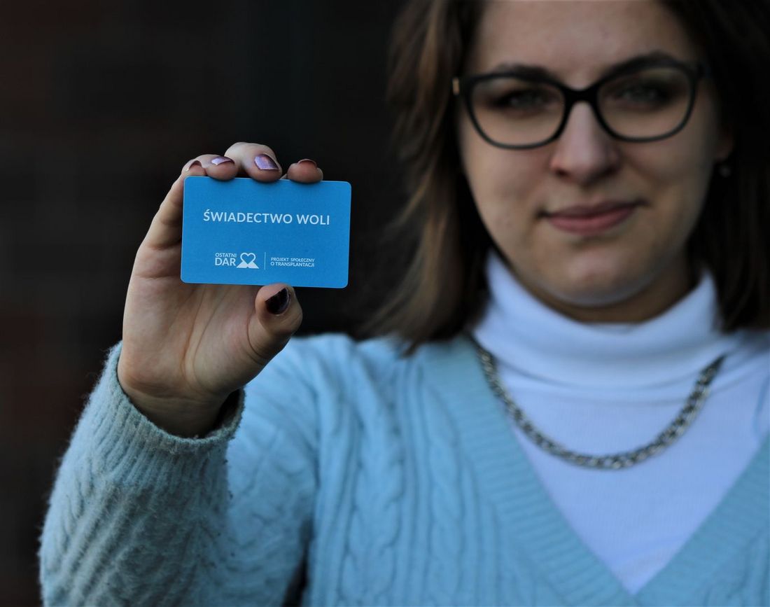 Zdjęcie przedstawiające panią która pokazuję karte świadectwo woli.