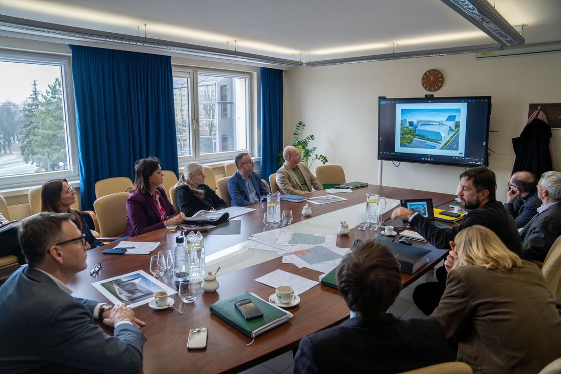 uczestnicy spotkania siedzą w sali przy stole konferencyjnym i oglądają projekcje na telewizorze