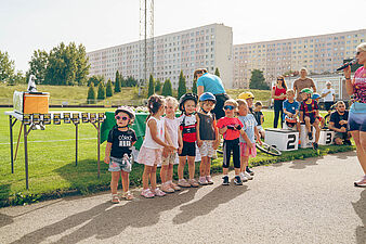 Dzieci stoją w równym rzędzie na tle boiska, czekając na oficjalne wręczenie medal i nagród