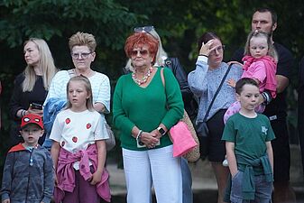 Zgromadzona publiczność, w tym dorośli i dzieci, uwanie ogląda plenerowy spektakl Teatru Cordis.