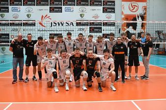 Pozująca do zdjęcia drużyna z trenerami na tle siatki