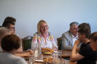 Uśmiechnięta kobieta w kwiecistej sukience siedzi przy stole obok mężczyzny w szarej marynarce