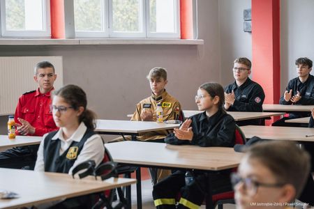 Szersza perspektywa na siedmioro uczestników konkursu siedzących przy stolikach