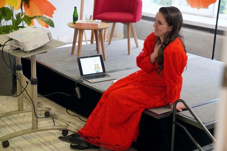 Sonia Białek siedzi na podeśćie w czerwonej sukni obok niej laptop