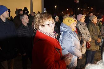 Profil uczestników spotkania plenerowego, w tym kobiety w czerwonym płaszczu i okularach na pierwszym planie