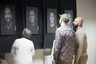 Kobieta w białym ubraniu wraz z dwoma mężczyznami oglądają galerię zdjęć portretowych