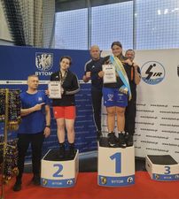 Zawodnczki stojące na stopniach podium, za nimi trenerzy.