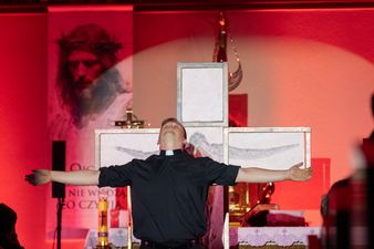 Tomasz Tuszyński w przebraniu Hanika na tle krzyża