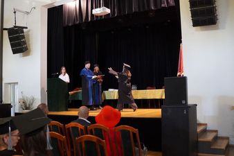 Rektor dr Andrzej Zduniak w błękitno-czarnej todze wręcza kartę absolutoryjną studentce na scenie. Obok stoi dziekan mgr Mateusz Tkocz.