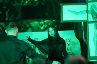 Kobieta w czarnej szacie rozkłada ręce w geście zaproszenia, w tle tablica z dekalogiem oraz krzyżem