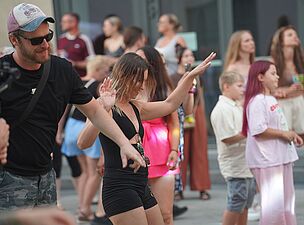 Kobieta w czarnym, krótkim komplecie tańcząca z podniesionymi rękami na placu imprezowym