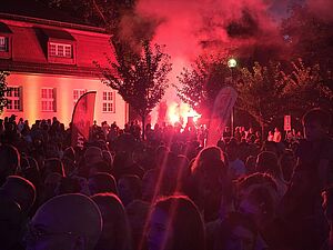 Tłum ludzi zgromadzony nocą na imprezie plenerowej oświetlony czerwoną flarą