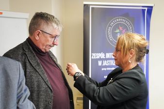 Członek Zespołu Interdyscyplinarnego przypina białą wstążke Wiceprezydentowi