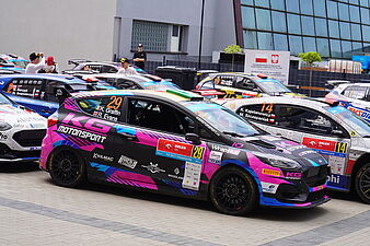 Czarno-różowy Ford Fiesta z numerem 29 zaparkowany w rzędzie z innymi autami rajdowymi
