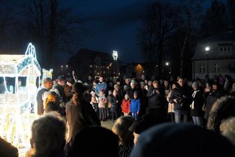 Zgromadzona nocą publiczność, w tym dzieci, słucha zespołu muzycznego występującego przy rozświetlonej dekoracji