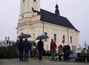 Osoby z parasolami na tle kościoła p.w. Wszystkich Świętych