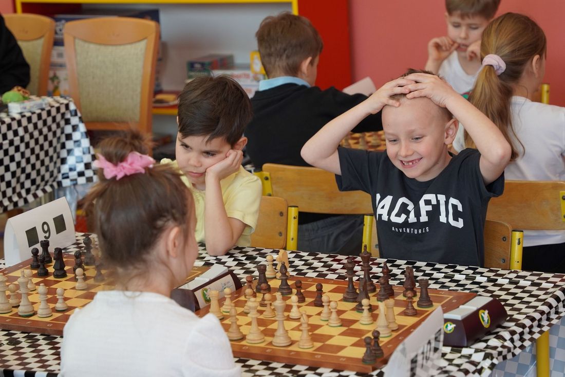 Uśmiechnięty chłopiec łapiący się za głowę przy partii szachów
